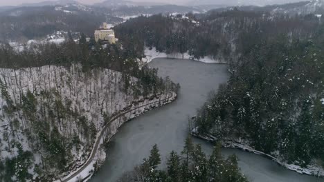 revealing shot of frozen lake surrounded with forest and fairy tale castle in the distance at winter