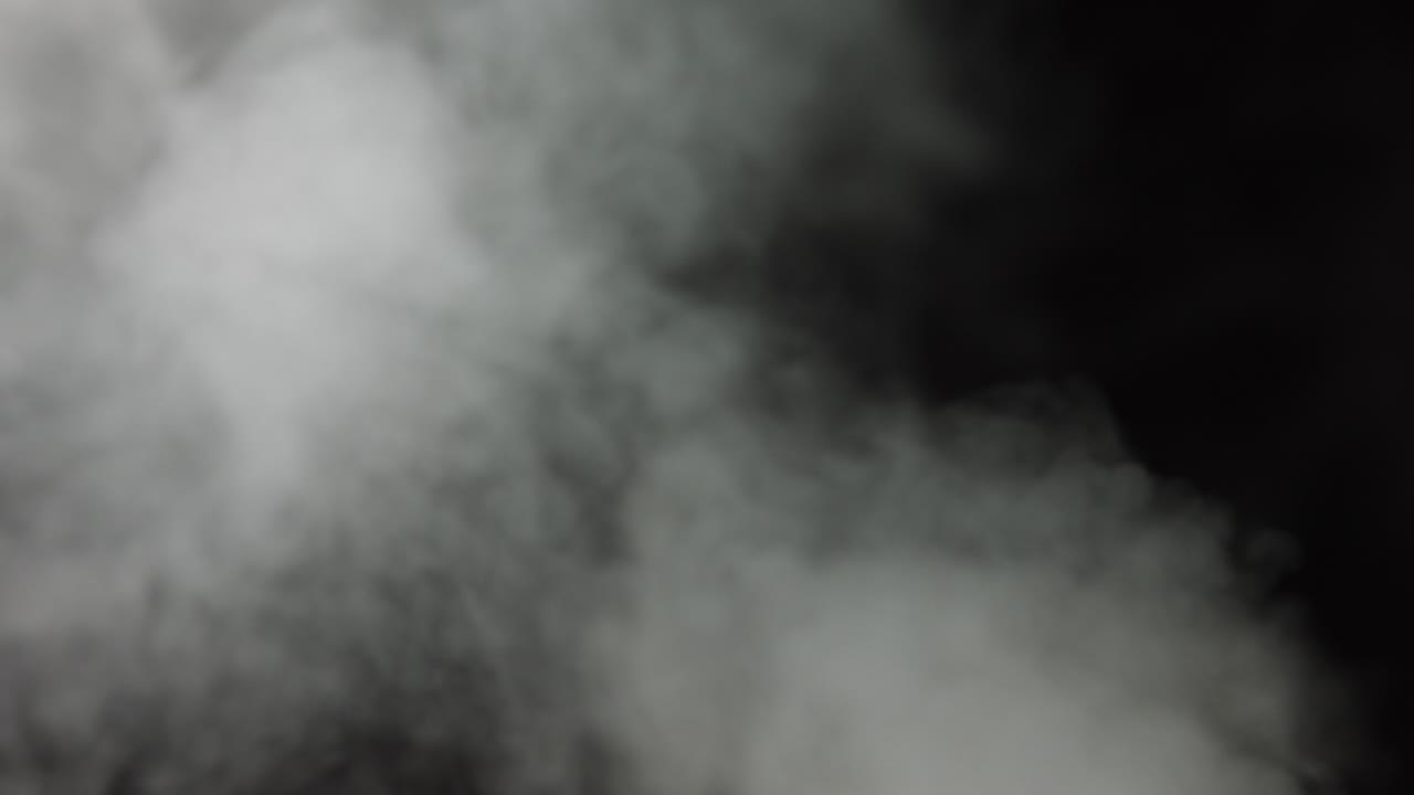 Atmospheric smoke VFX overlay element. Haze background. Smoke in slow motion on black background. White smoke slowly floating through space against black background. Mist effect. Fog effect