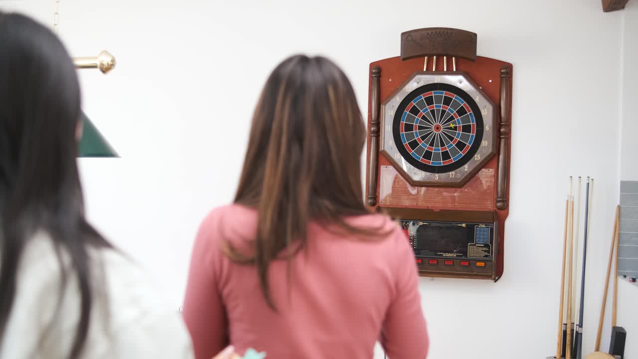 Woman throwing dart arrows at target of dartboard at home