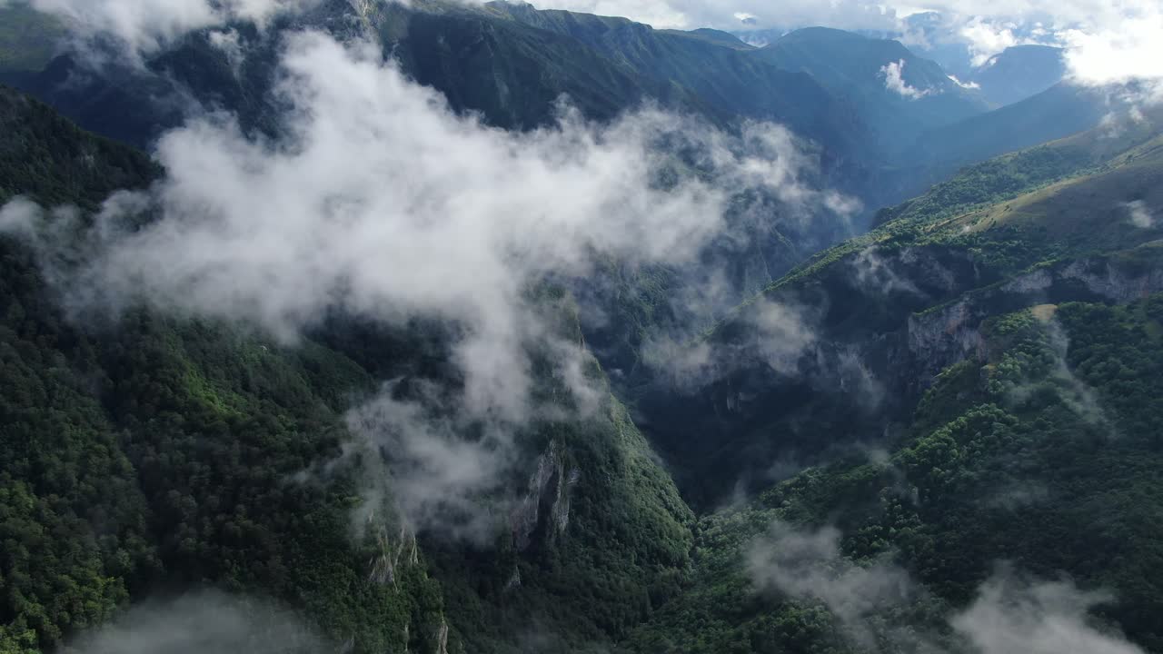 A view of forested mountains and cliffs partially obscured by low lying clouds The terrain appears steep with deep valleys visible