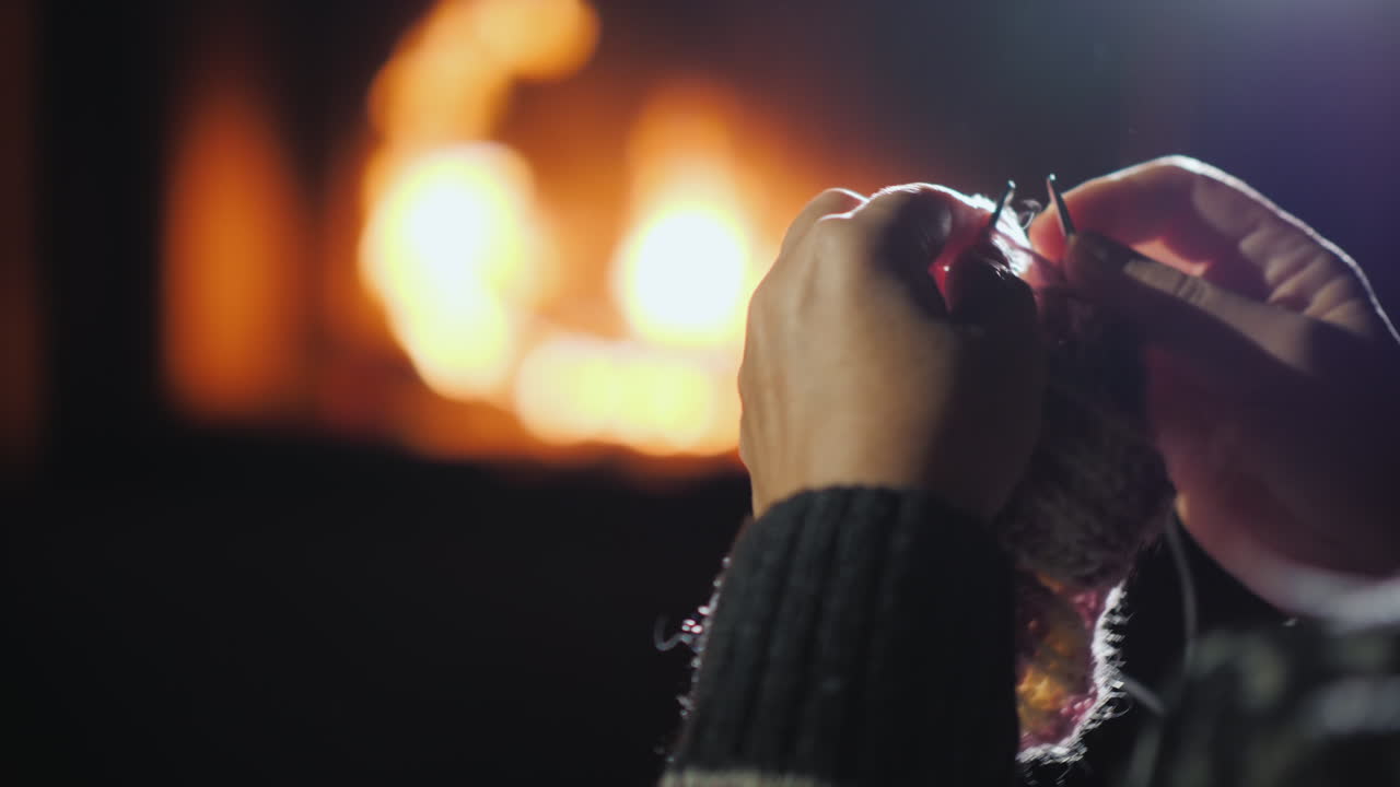 una mujer teje ropa de abrigo en el marco de las manos con agujas de tejer son visibles en el fondo de