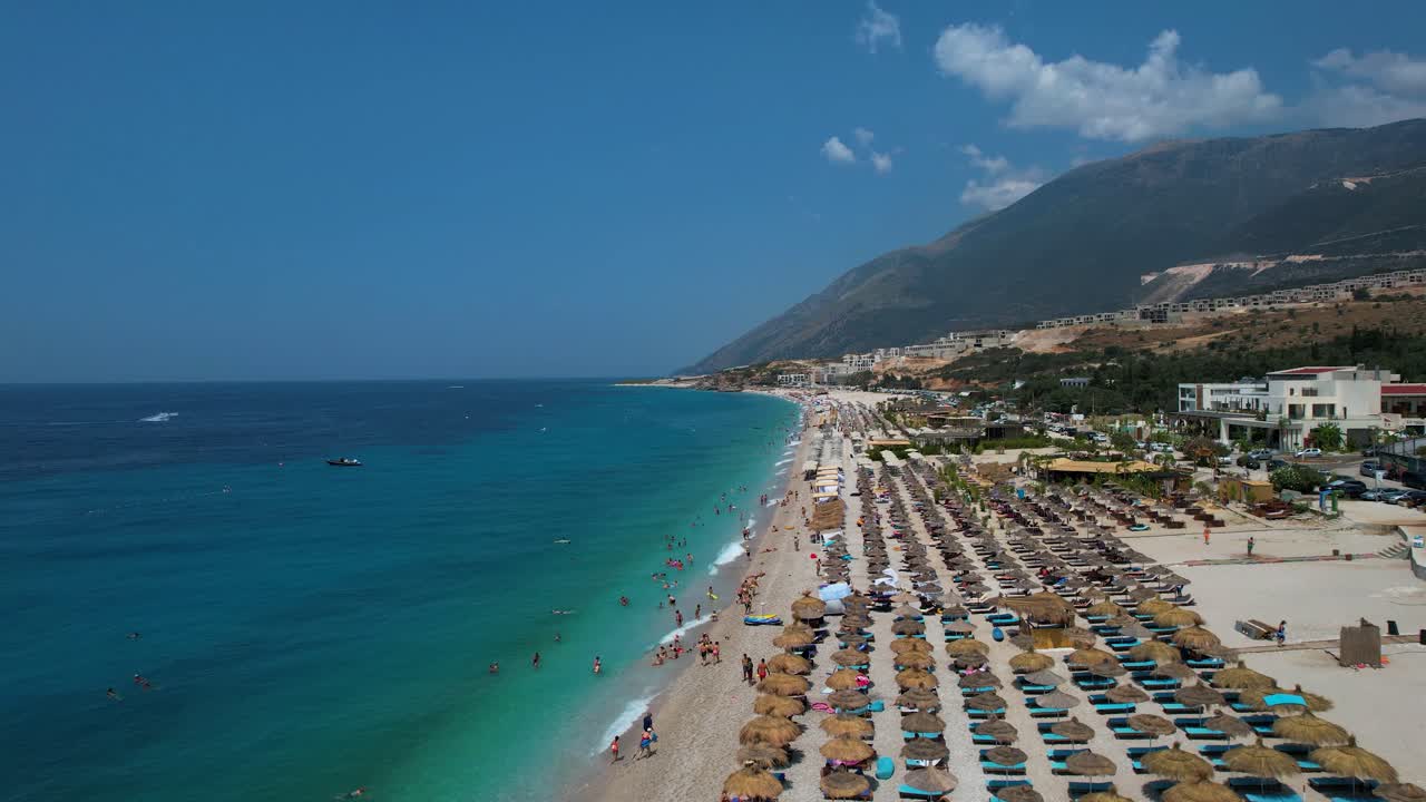 Sunbathers Relax Under Umbrellas on the Vast Ionian Coast Beach with Clear Blue Waters in Drimadhes, Albania