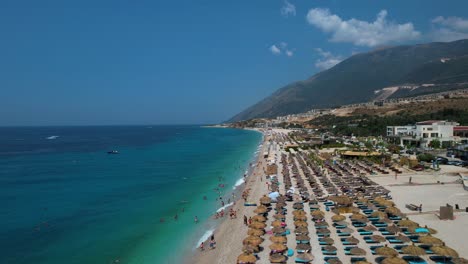 Los-Bañistas-Se-Relajan-Bajo-Las-Sombrillas-En-La-Amplia-Playa-De-La-Costa-Jónica-Con-Aguas-Cristalinas-En-Drimadhes,-Albania.