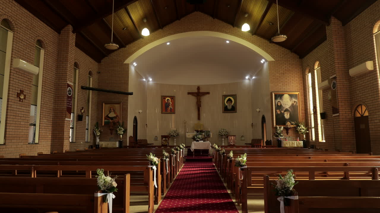 Panning shot of aisle of an empty church with wooden pews - cross