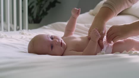 unrecognizable mother changing diaper of a newborn lying on the bed