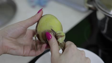 las manos de la ama de casa pelando patatas en la cocina.