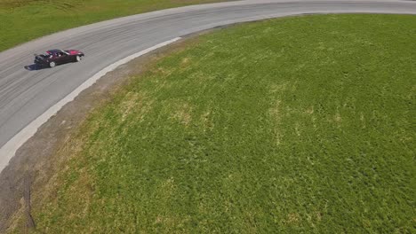 toma aérea de un auto verde que circula a alta velocidad en un giro, hierba verde y una pista de carreras, toma de seguimiento en la parte superior
