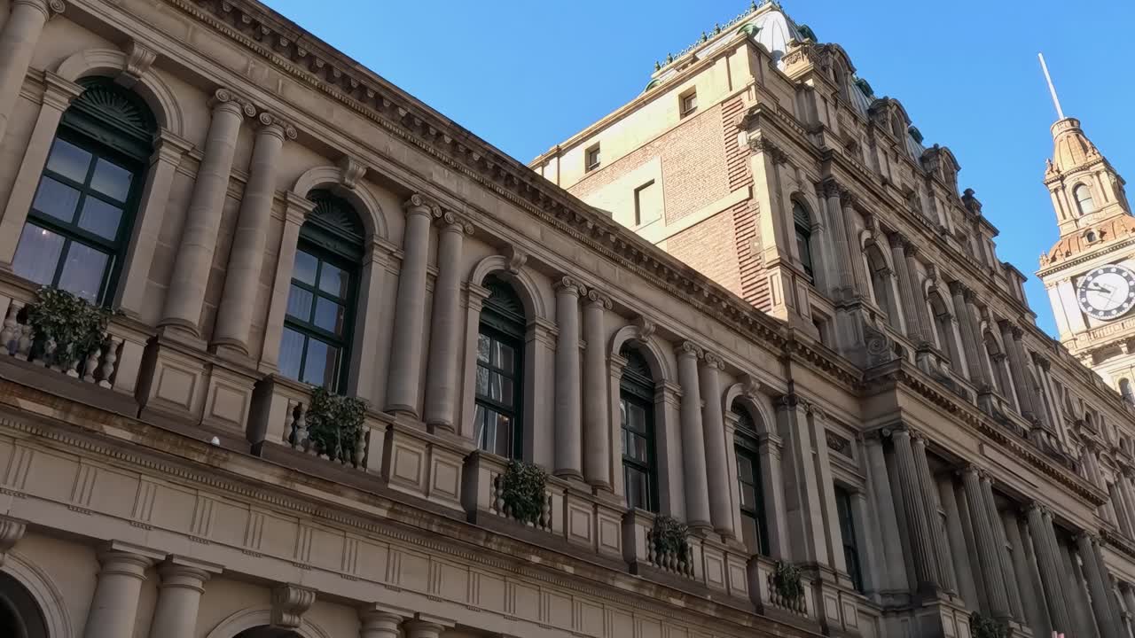 View of a historic clock tower, modern skyscrapers, and leafy trees under a clear blue sky.