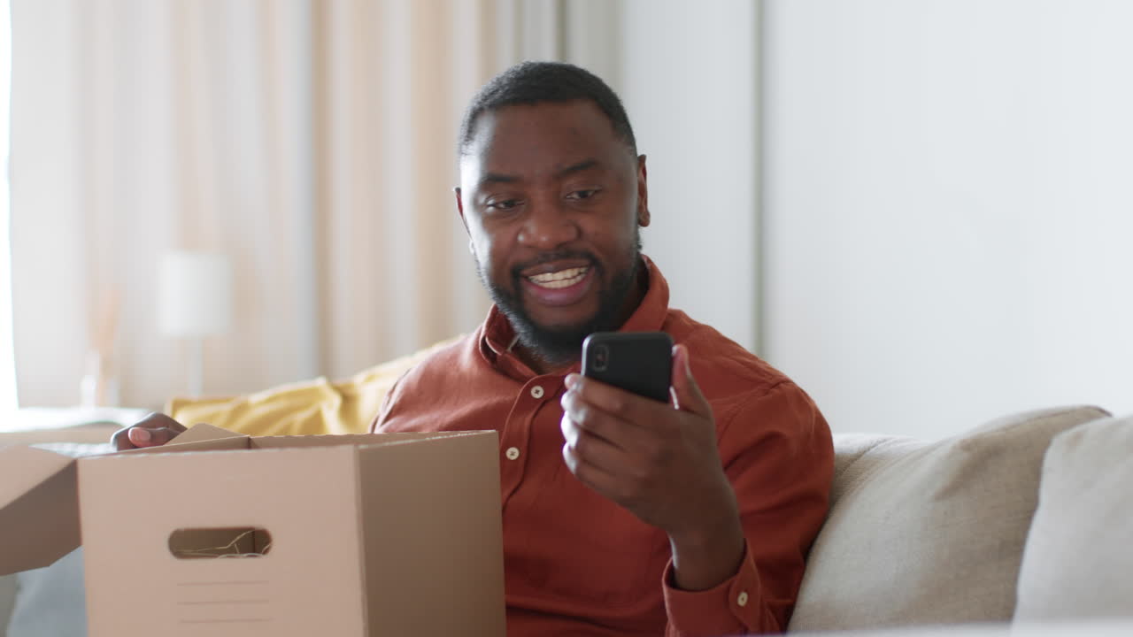 Man unpacking a cardboard box and using a smartphone