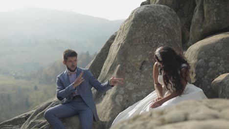 el novio y la novia se sientan en una ladera alta de la montaña.