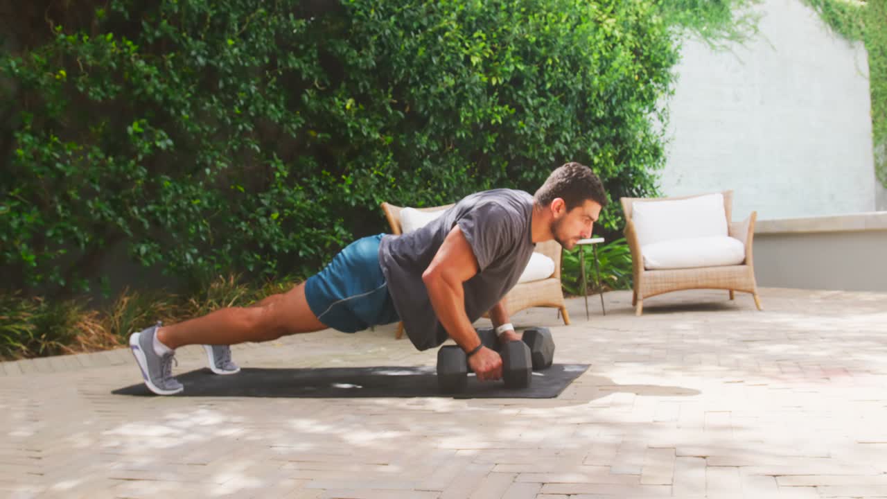 Uomo che esegue flessioni plank e rematore con manubrio esagonale a braccio singolo su un tappetino da esterno, indossando abbigliamento sportivo.