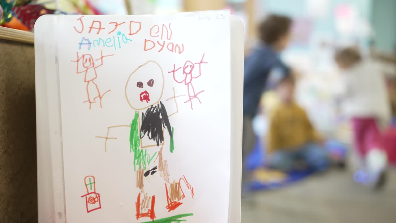 A preschooler's drawing hung up with unidentifiable children playing in background