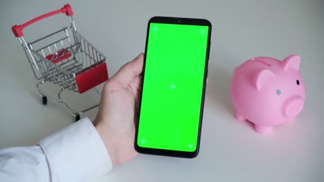 teléfono con una pantalla chromakey en las manos de un primer plano. vista superior de la caja de ahorros del teléfono inteligente y el carrito de compras copia el espacio sobre fondo blanco