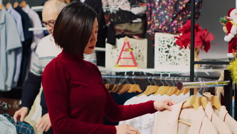 Frau-Stöbert-Durch-Elegante-Blazer-Auf-Regalen-In-Einem-Weihnachtlich-Geschmückten-Einkaufsladen-Und-Ist-Auf-Der-Suche-Nach-Der-Perfekten-Kleidung-Für-Das-Weihnachtsessen.-Modischer-Kunde,-Der-Neue-Kleidung-Braucht