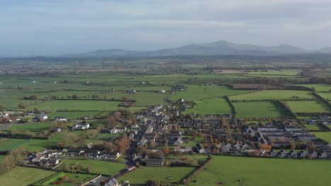 a tilting aerial shot revealing a small irish town nestled into the lush green rolling hills of the ireland countryside