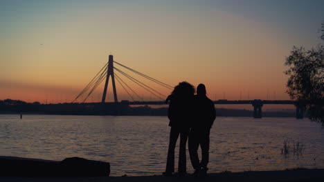 lovers silhouette watching sunset at river shore. beautiful evening clear sky.