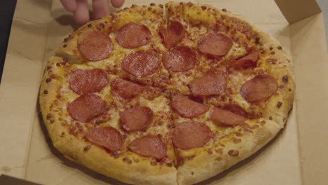 mano agarrando una rebanada de pizza de pepperoni que se agarra de toda la pizza - medio