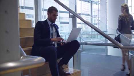 Businessman using laptop on stairs in the office 4k
