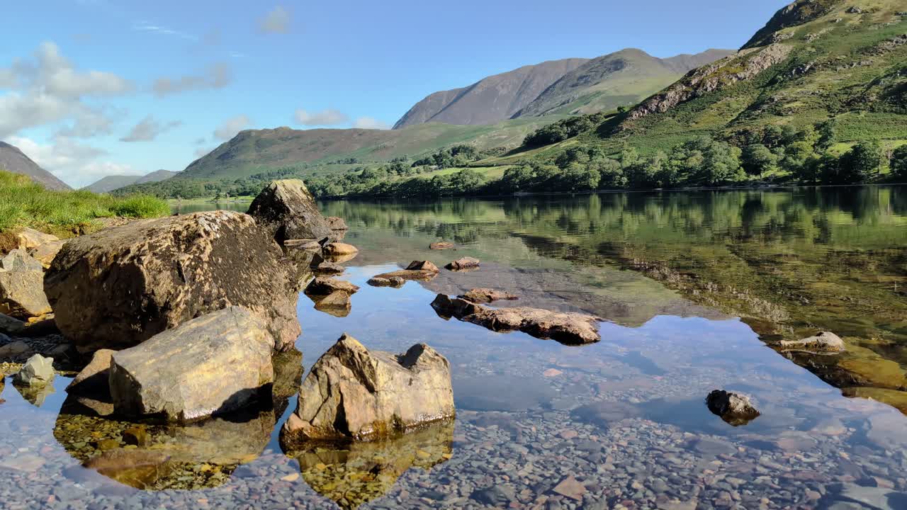 views of Buttermere Lake on a bright, sunny day. The calm water reflects the iconic Lake District fells