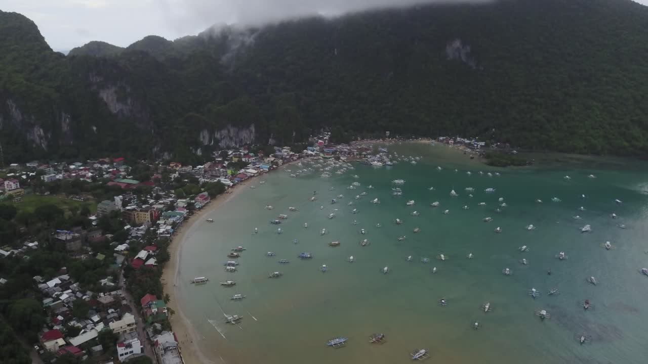 Quang cảnh từ trên cao bằng máy bay không người lái của vịnh với nhiều thuyền và thị trấn ven biển dưới bầu trời nhiều mây ở El Nido, Palawan, Philippines.