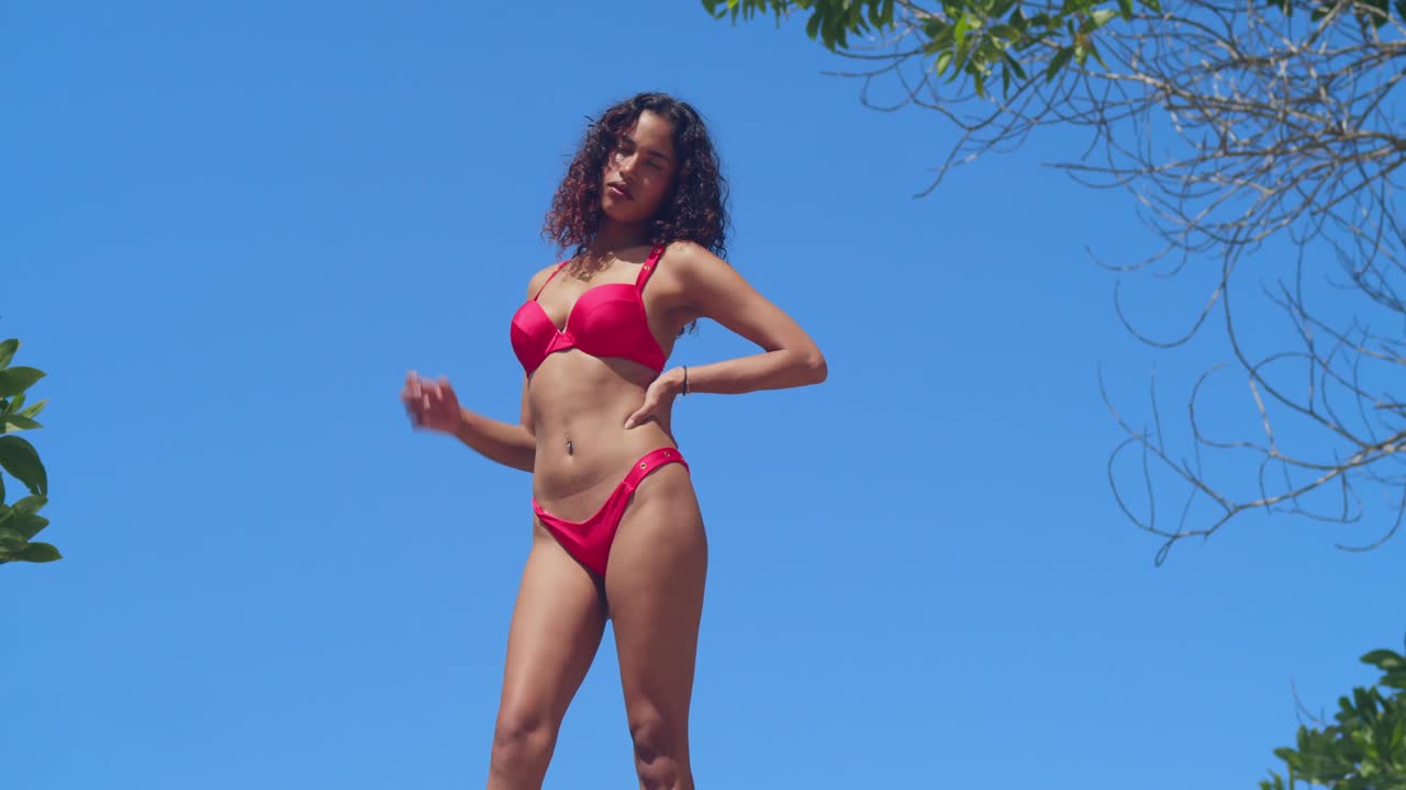 In una giornata soleggiata, una giovane donna in bikini rosso si rilassa su un muro in una fortezza panoramica su un'isola ai tropici