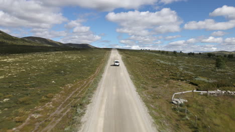 Drone-capture-the-vehicle-which-driving-in-front-on-the-isolated-with-green-covered-land-on-both-and-numerous-hills-can-be-seen-on-the-side