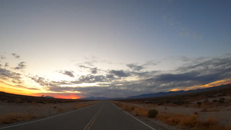 driving along a mojave desert road towards the mountains and sunset - driver point of view