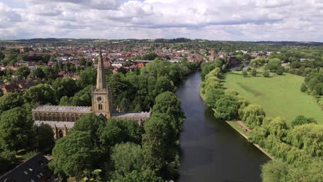 Vista-Aérea-Del-Carro-A-Través-De-La-Iglesia-De-La-Santísima-Trinidad-Y-El-Río-Avon-Tranquilo-Paisaje-Suburbano-De-Warwickshire