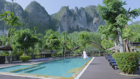 lady in summer dress on vacation at thai resort walks barefoot next to pool