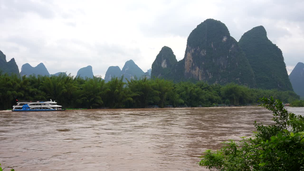 Cruise ship navigates Lijiang river brown waters along karst mountains in Xingping, China
