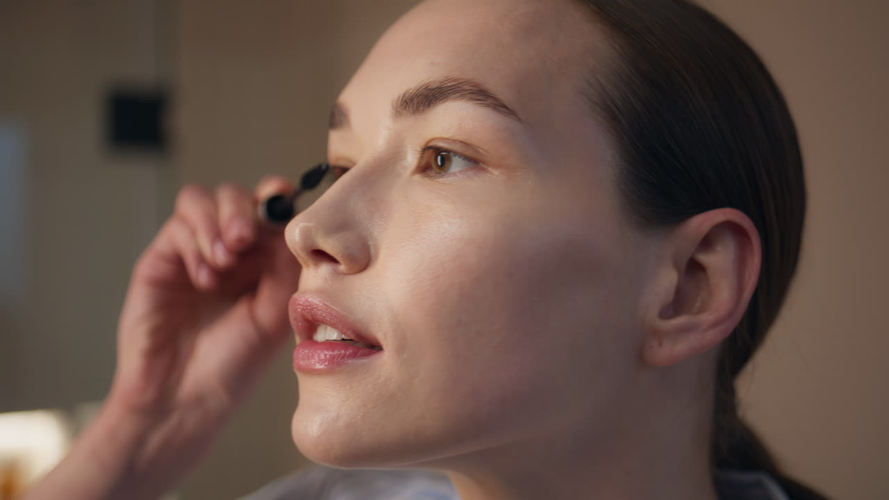 Woman applying black mascara in bathroom light closeup. Pretty lady doing makeup
