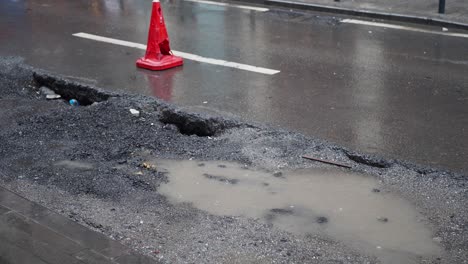 a road with a large pothole and a traffic cone warning drivers.