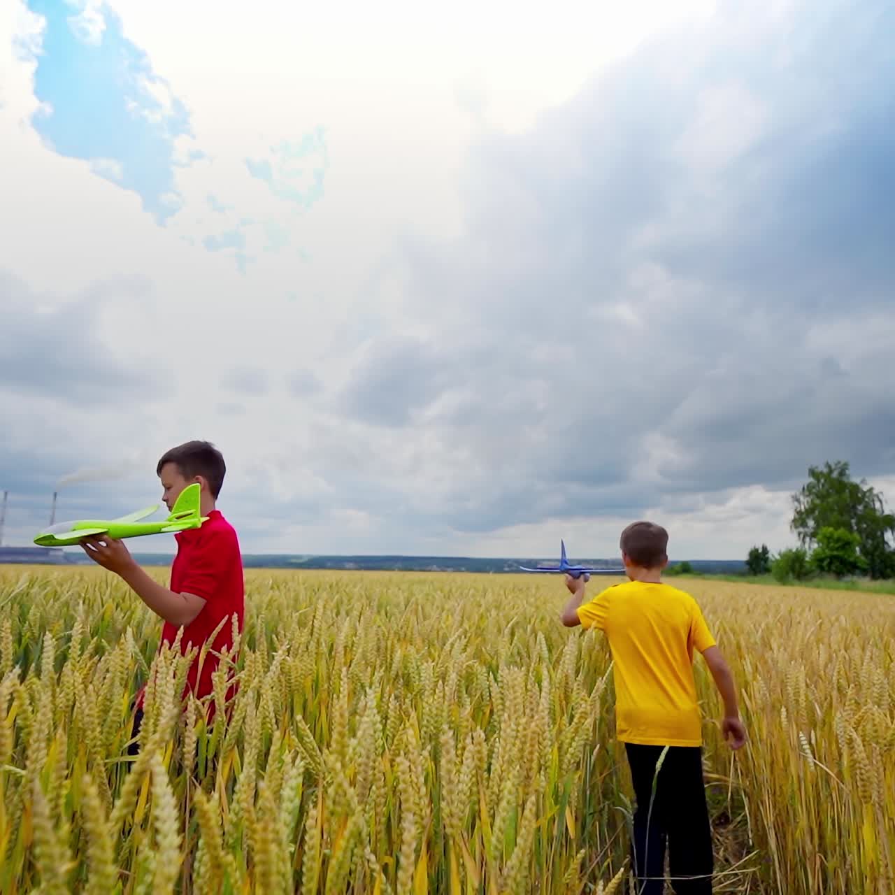 Two happy boys playing with toy plane in wheat field. Cloudy sky. Video of playing process. Summer and vacation concept.