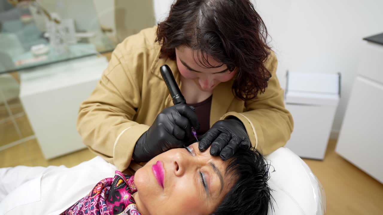 Kosmetikerin trägt Permanent Make-up für Augenbrauen bei einer Kundin im Schönheitssalon auf.