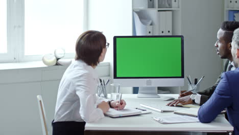 Multi-Ethnic-Group-Of-Professional-Businessmen-And-Businesswoman-Sitting-At-Office-Table,-Writing-Down-Notes-And-Discussing-Ideas-Via-Video-Call-On-Computer-With-Chroma-Key-Screen