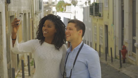 smiling multiracial couple taking selfie on street.