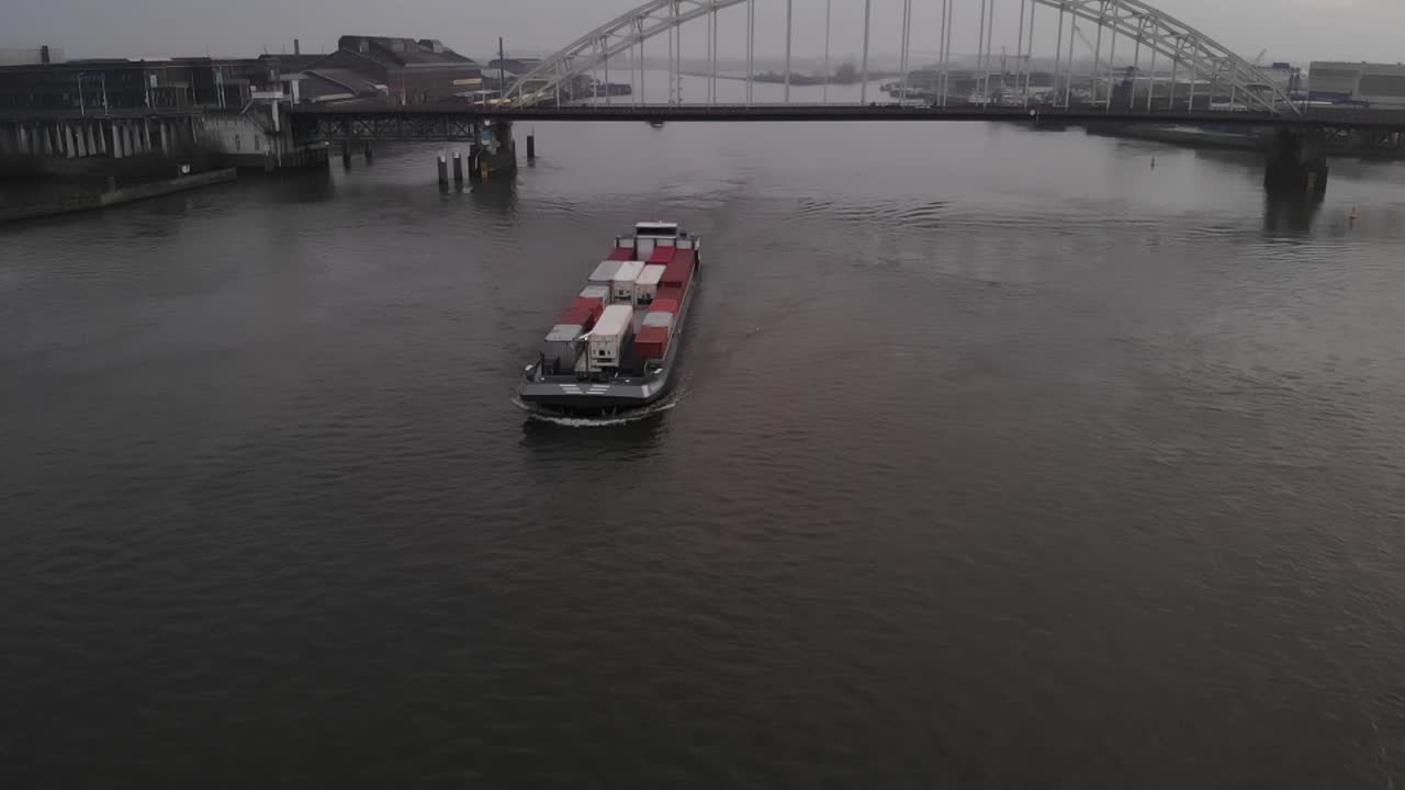 Dutch cargo barge loaded with containers navigating on a dutch river Noord with a bascule bridge on the background. Drone truck shot