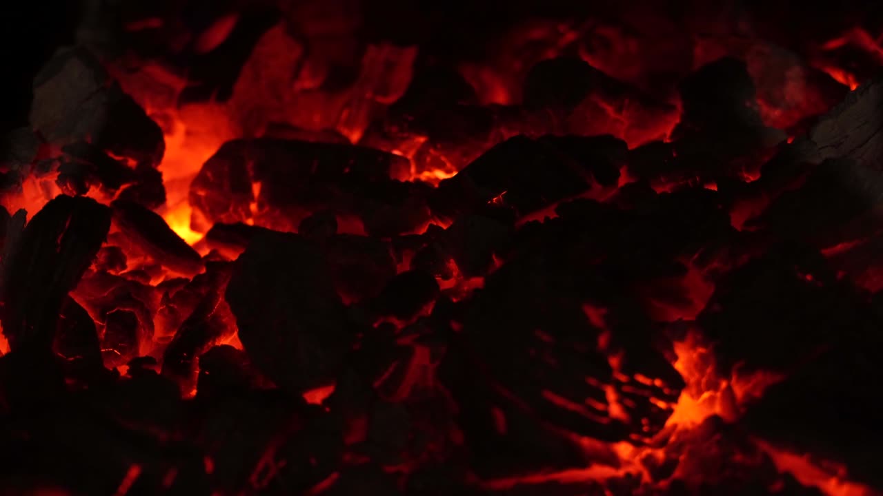 Red-hot coals burn in the fireplace. The flame of the fire burns slowly in the furnace. A burning fireplace. Flaming burning sparks close-up, fire patterns. Infernal glow of fire in the dark