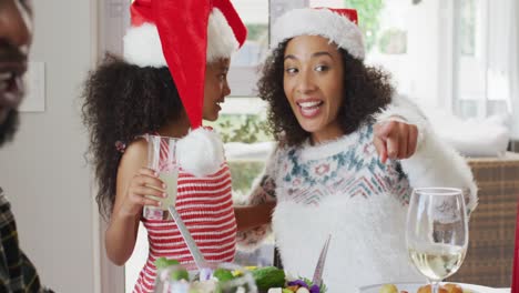 Happy-african-american-mother-and-daughter-wearing-santa-hats-and-celebrating-in-kitchen