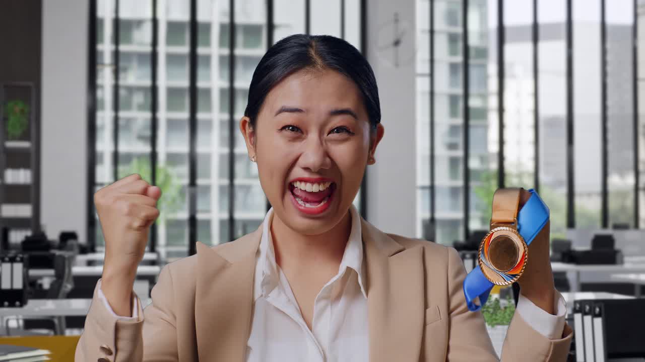 Close Up Of Asian Business Woman In A Suit Looking At A Gold Medal Then Screaming Goal Celebrating Winning As The First Winner In The Office