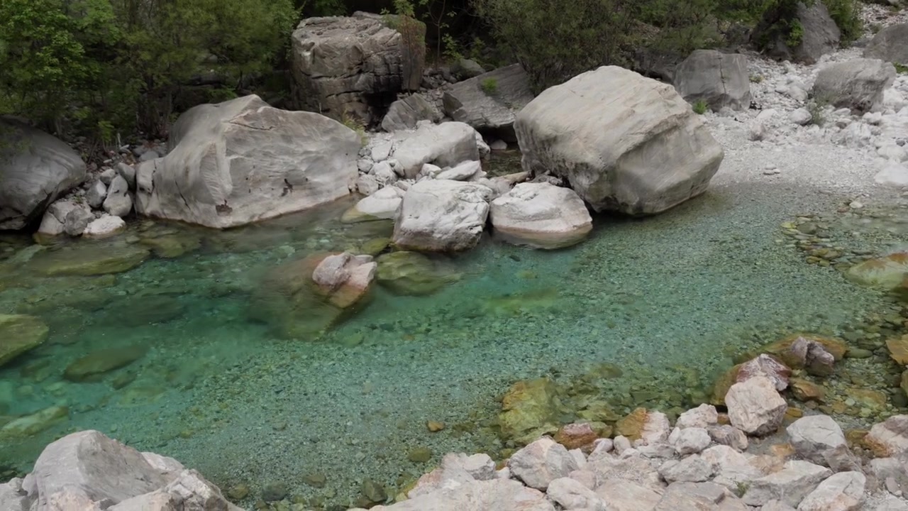 Un sereno fiume turchese si snoda tra grandi rocce bianche e una lussureggiante foresta verde nella valle di Valbona in Albania, catturando la bellezza naturale e un'atmosfera calma.