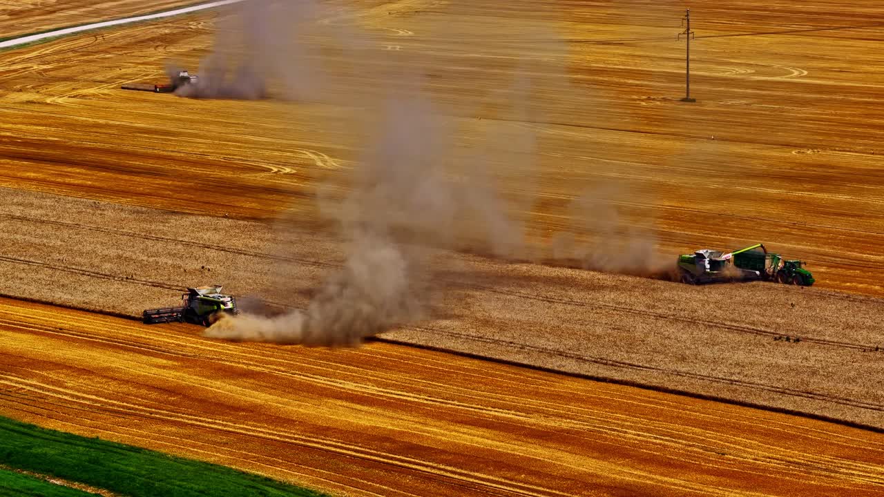 Tractor combine kicks up dust and smoke while working dry farmland, wide aerial orbit of harvest scene