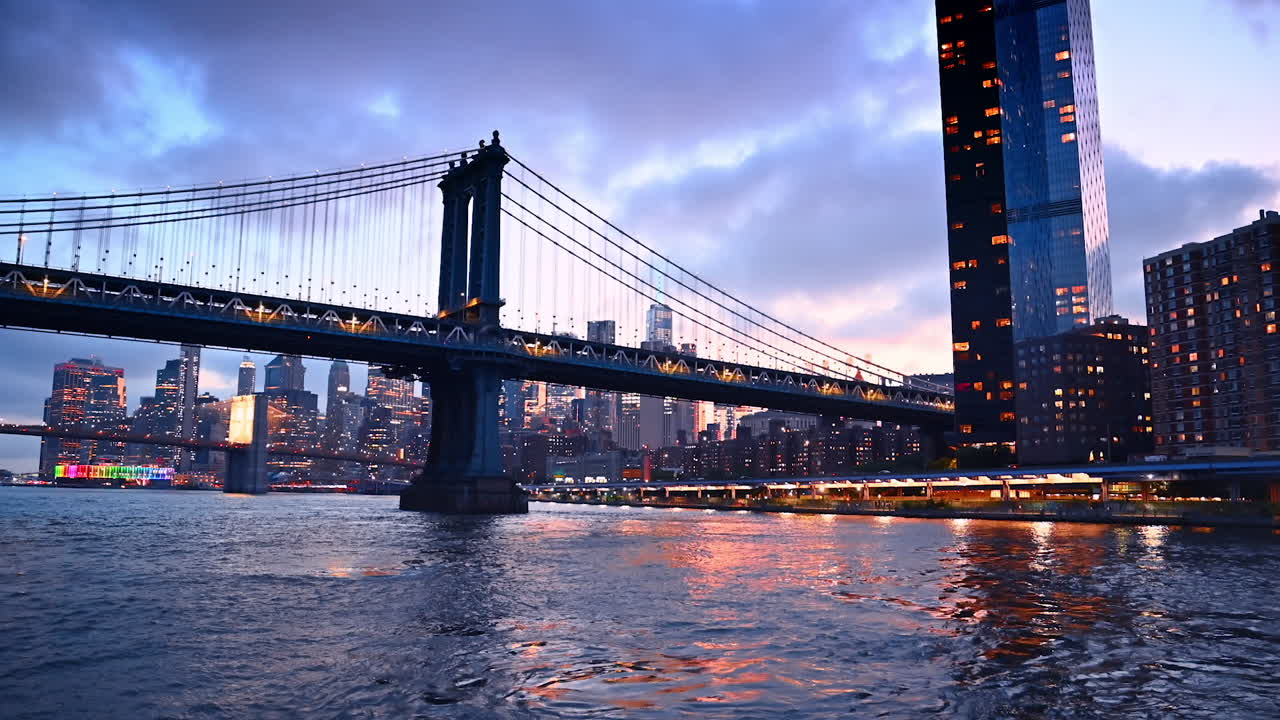 Moving by the East River waterscape near the waterfront. Low angle view at the Manhattan Bridge at the backdrop of grey overcast sky