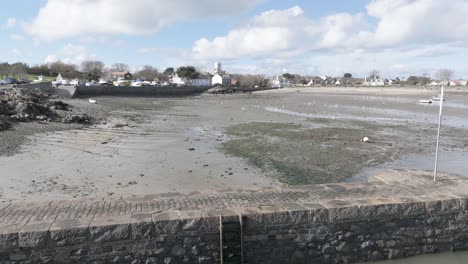 reveal of bordeaux harbour guernsey at low tide with harbour wall, boats drying out on sand,beach and cottages in the background on a bright day