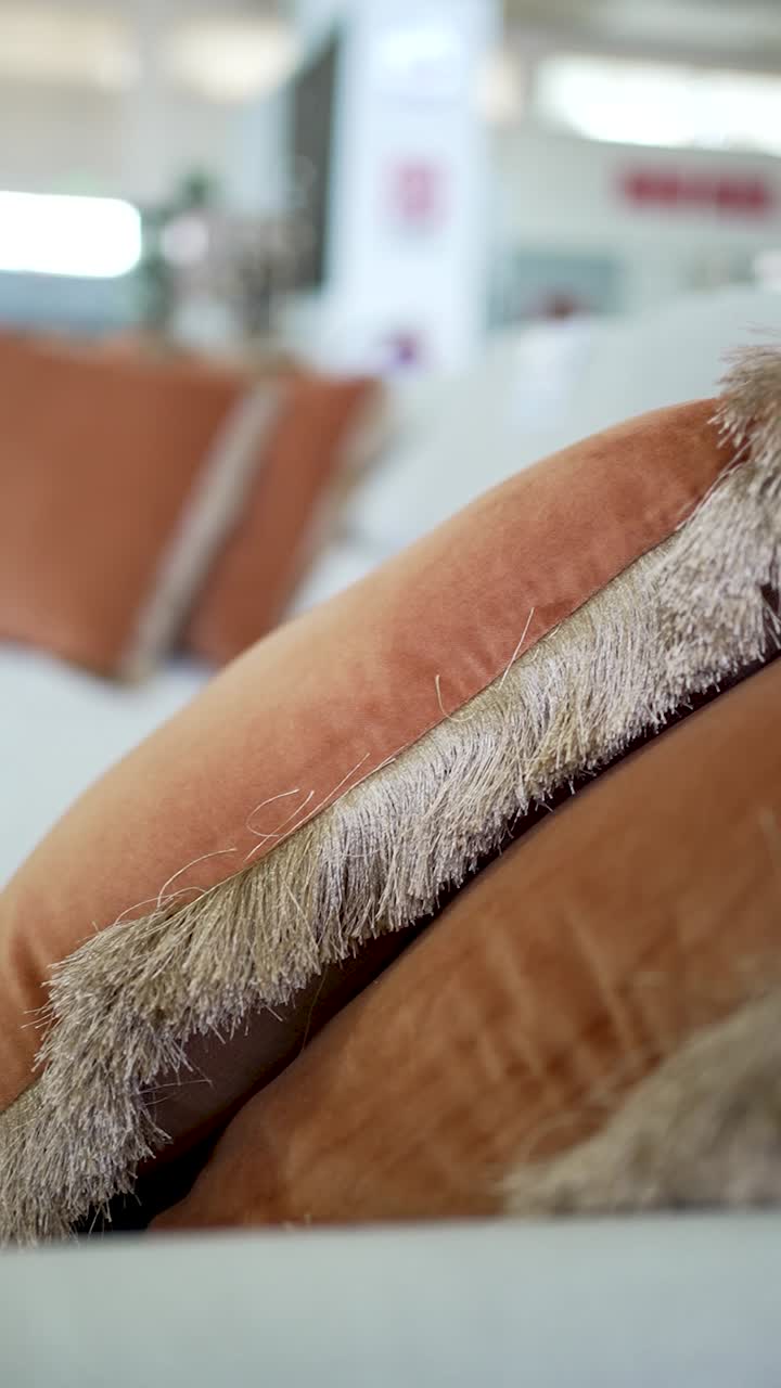 Close view of plush decorative pillows featuring a warm orange color and soft fringe. They create a comfortable and inviting atmosphere in a cozy living room, illuminated by afternoon sunlight