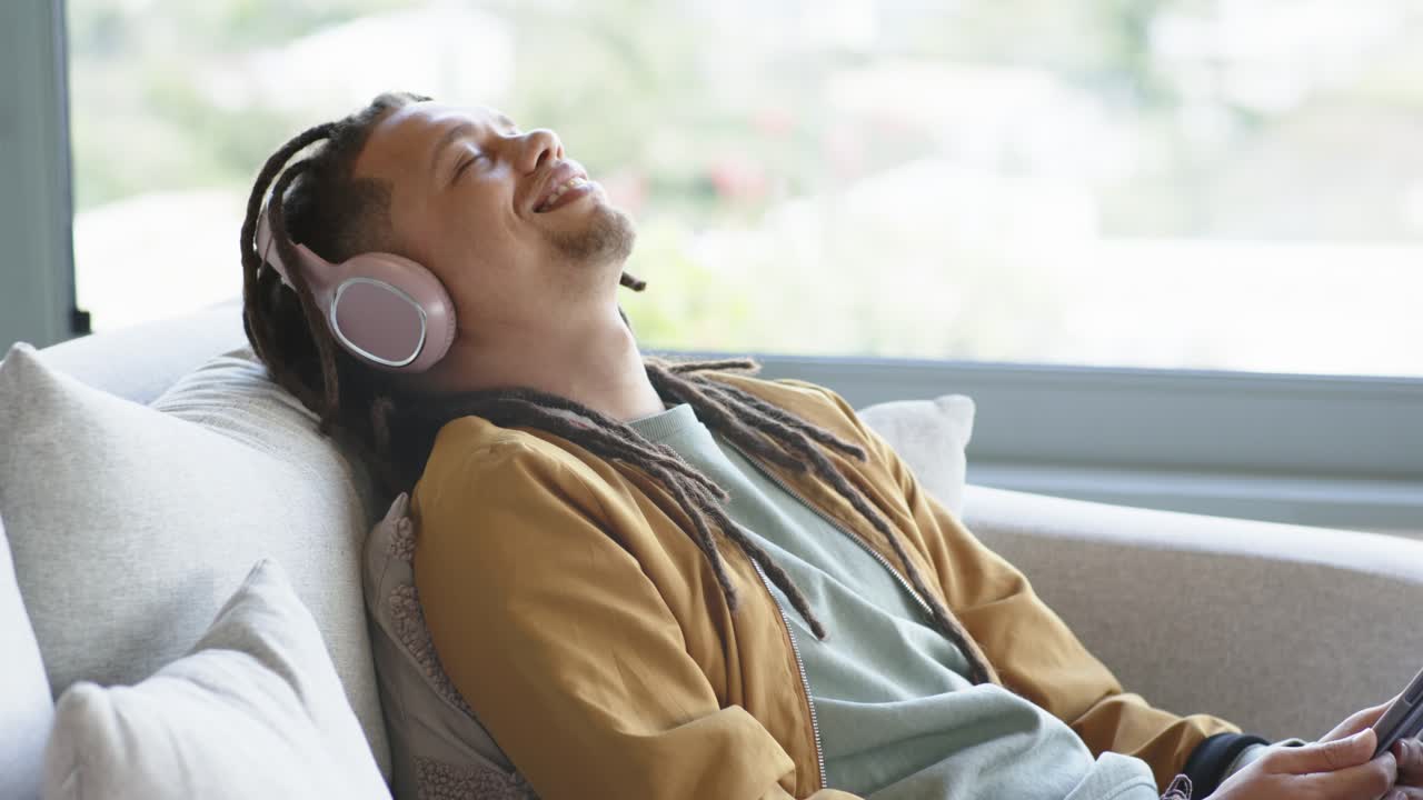 Uomo che tocca lo schermo di un tablet e si rilassa su un divano mentre ascolta musica con cuffie wireless