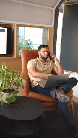 vertical video: working from home, man using laptop and making phone call in living room