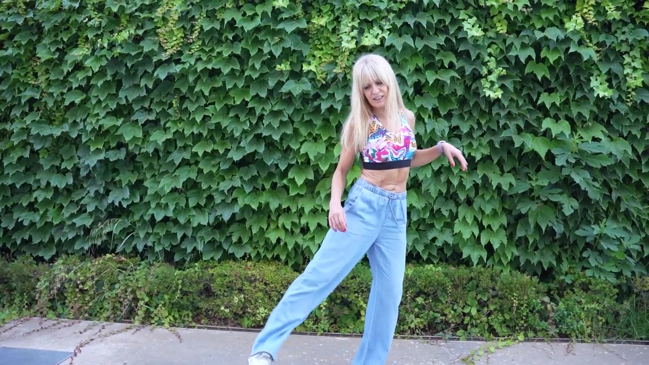 A young woman wearing casual clothing is striking a pose in front of a green ivycovered wall