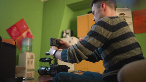 person reaching into camera bag, adjusting camera equipment in home studio. preparing gear for video shoot, with camera, microphone, and accessories on table in creative workspace