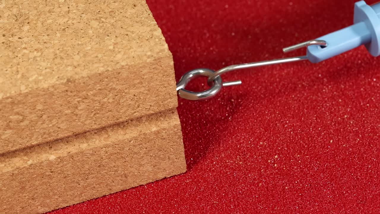 A hand uses a spring scale to measure friction on a wooden block over sandpaper, demonstrating force dynamics